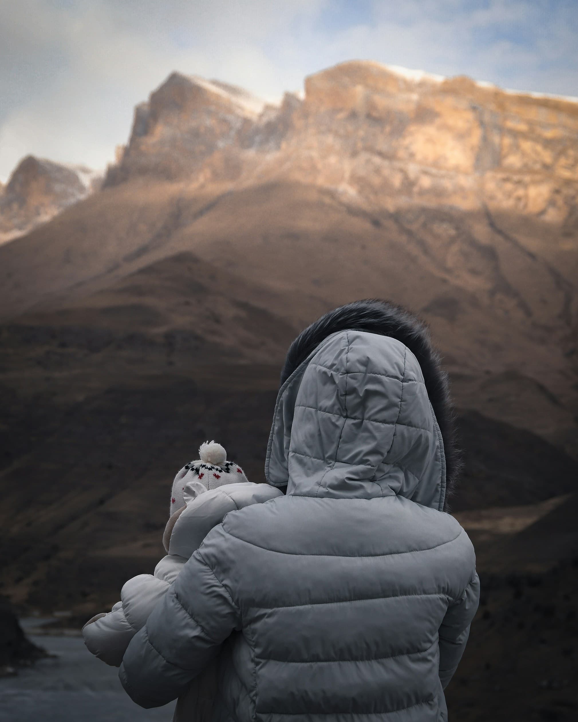 A person holding a child overlooking a sunny mountain cliff